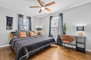 A bedroom with a bed, a desk, a chair, a ceiling fan, and a window with curtains. - Boho Lounge - Pet Friendly Home Close to I-35 & KC (Merriam)