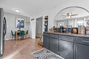 A modern kitchen with dark cabinets, a dining area with a table and chairs, and a ceiling fan. - Boho Lounge - Pet Friendly Home Close to I-35 & KC (Merriam)