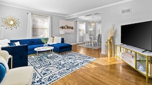 Una sala de estar moderna con un sofá azul, sillones blancos, una mesa de centro y un televisor de pantalla plana grande.