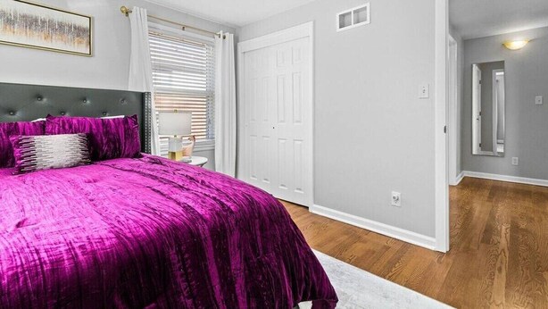 A bedroom with a large bed, a nightstand, a window with blinds, a door, and a hallway. - Kansas City Townhouse Walk to Plaza+Streetcar 1006 (Kansas City)