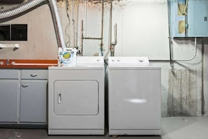 A laundry area with two white washing machines, a bottle of All Clear, and a blue utility box.
