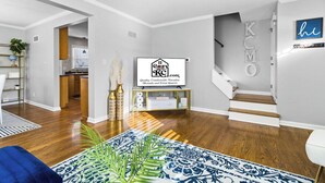 A modern living room with hardwood flooring, a blue patterned rug, a television, and a staircase. - Kansas City Townhouse Walk to Plaza+Streetcar 1006 (Kansas City)