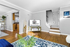 Una sala de estar moderna con pisos de madera, un tapiz azul estampado, un televisor y una escalera.
