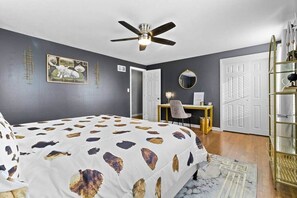 A bedroom with a bed, a desk, a chair, a ceiling fan, and a bookshelf.