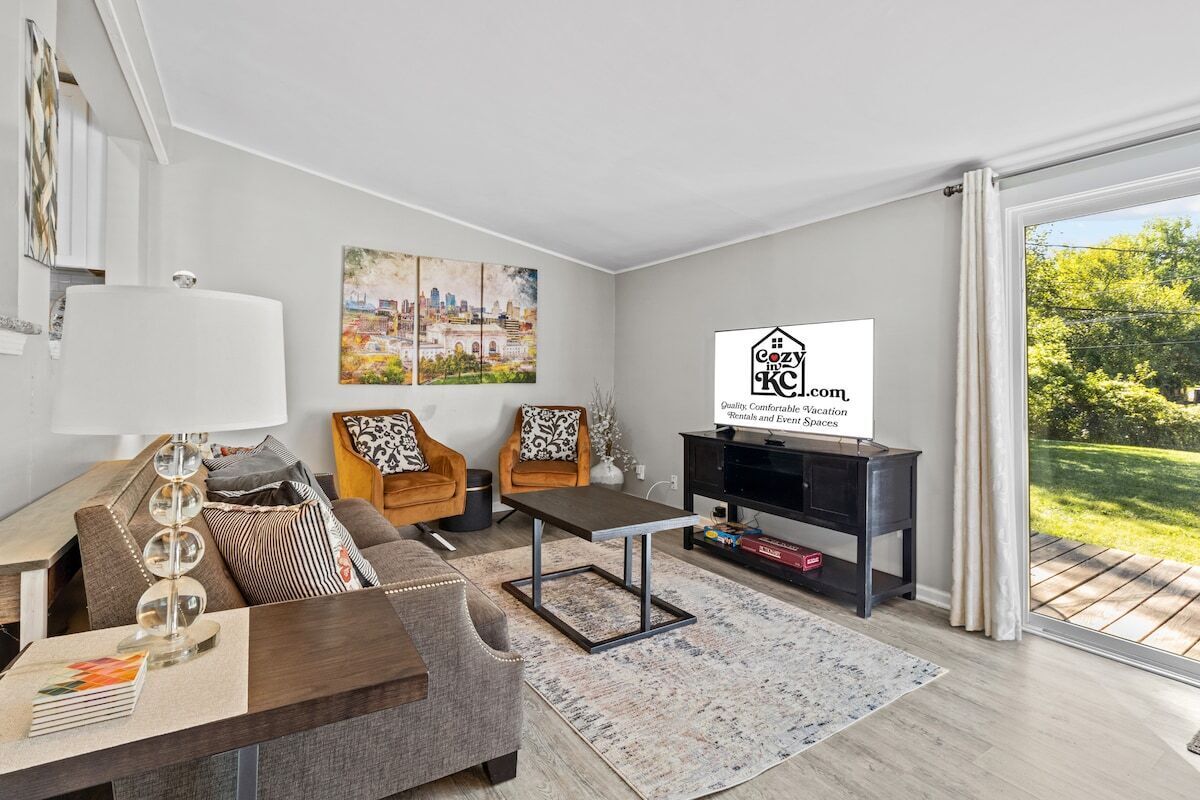 Een moderne woonkamer met een bank, fauteuils, een salontafel, een televisie en een schilderij van een stadsgezicht.