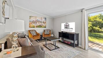Een moderne woonkamer met een bank, fauteuils, een salontafel, een televisie en een schilderij van een stadsgezicht.