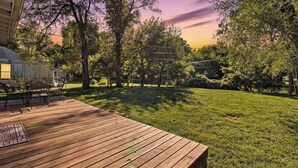 A wooden deck with a table and chairs, surrounded by a grassy lawn and trees.