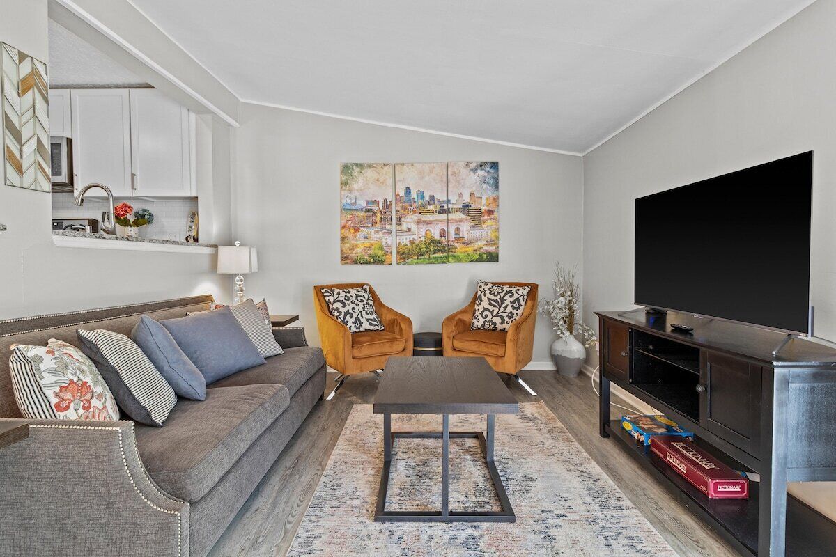 Ein Wohnzimmer mit einer Couch, zwei Sesseln, einem Couchtisch, einem Flachbildfernseher und einem Gemälde an der Wand.