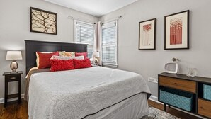 A bedroom with a bed, bedside tables, a dresser, and artwork on the walls.