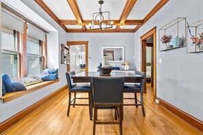 A dining room with a wooden table and chairs, a chandelier, and a large window with a view.