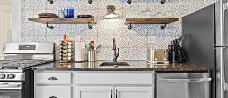 Una cocina con armarios blancos, electrodomésticos de acero inoxidable y estantes decorativos de madera.