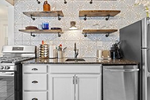 Una cocina con armarios blancos, electrodomésticos de acero inoxidable y estantes decorativos de madera.