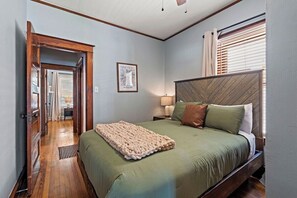 A bedroom with a bed, a wooden headboard, a framed picture on the wall, and a door leading to another room. - KC Nest - Walkable to Plaza + Parking + Streetcar (Kansas City)