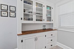 A kitchen with white cabinets, a wooden countertop, and a window with blinds.