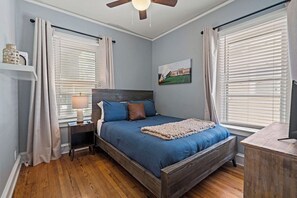 A bedroom with a bed, bedside table, lamp, and a painting on the wall.