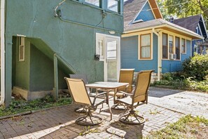 A patio with a table and four chairs, a door, and a blue house in the background.