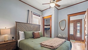 Un dormitorio con cama, mesita de noche, lámpara, ventilador de techo y una puerta que da a otra habitación.