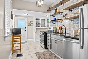 A modern kitchen with stainless steel appliances, wooden shelves, and a patterned backsplash.