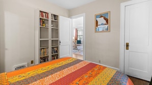 A bedroom with a large bed, a bookshelf, a door, and a framed picture on the wall. - Plaza Perch -Walk to Plaza & Westport! (Kansas City)