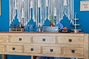 Un comptoir de bar en bois, avec un mur bleu en arrière-plan, décoré de suspensions en macramé et d’une pancarte de bienvenue.