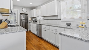 A modern kitchen with white cabinets, granite countertops, stainless steel appliances, and a wooden floor. - Plaza Perch -Walk to Plaza & Westport! (Kansas City)