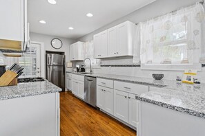 A modern kitchen with white cabinets, granite countertops, stainless steel appliances, and a wooden floor. - Plaza Perch -Walk to Plaza & Westport! (Kansas City)