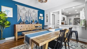 A dining area with a wooden table, black chairs, and a blue wall with a macrame decoration. - Plaza Perch -Walk to Plaza & Westport! (Kansas City)