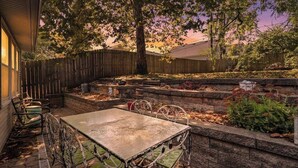 A patio area with a table and chairs, surrounded by a wooden fence and a garden bed with plants. - Plaza Perch -Walk to Plaza & Westport! (Kansas City)