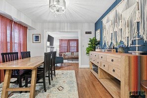 A dining area with a wooden table and chairs, a kitchen with a wooden cabinet, and a macrame wall hanging.