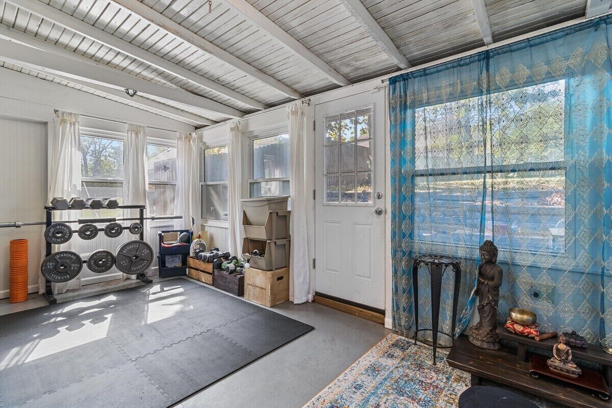 A room with a ceiling fan, a window with curtains, a door, and a small statue on a shelf.