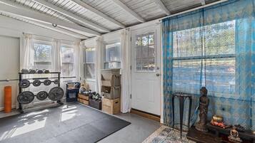 A room with a ceiling fan, a window with curtains, a door, and a small statue on a shelf.