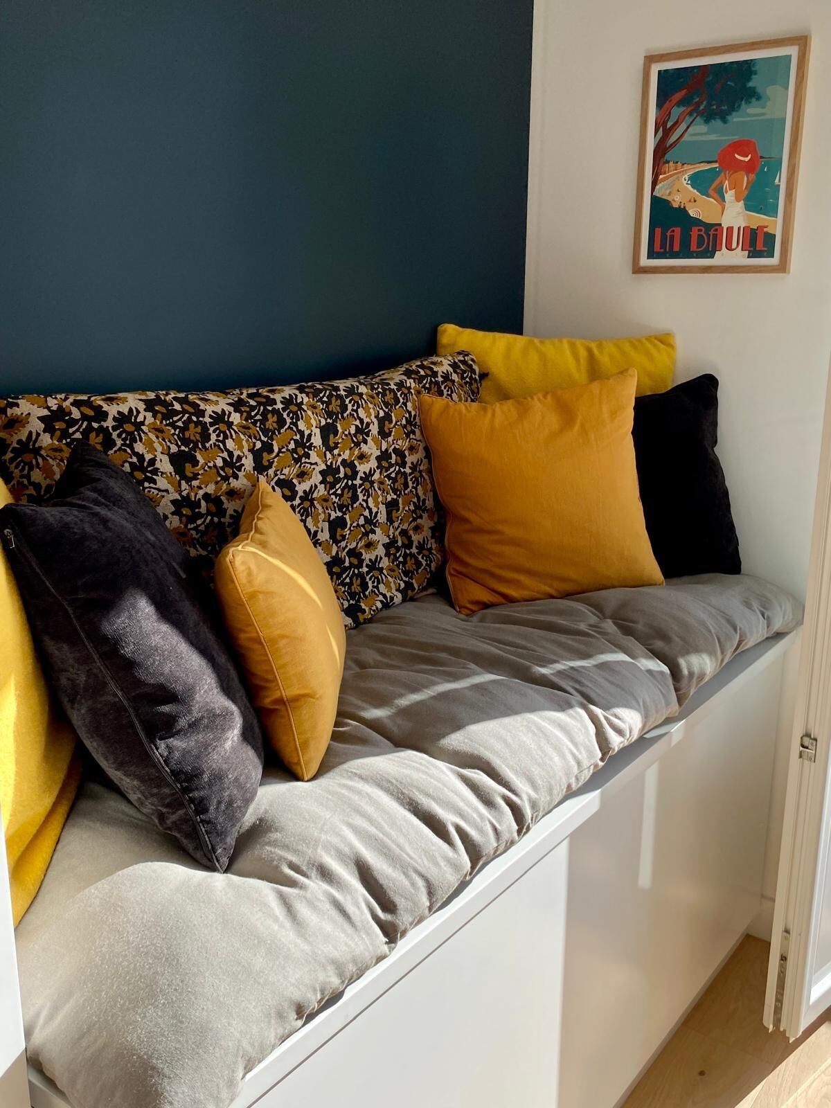 A sofa with multiple cushions in various colors, a framed picture on the wall, and a door leading to another room.
