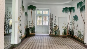 Een gang met decoratieve vloertegels, een witte deur met een raam en muren versierd met plantenmotieven.