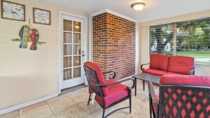 A patio area with a brick fireplace, red upholstered chairs, and a table. - Cottage Mins From Stadiums + Parking + Pet Welcome (Independence)