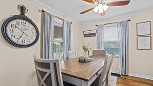 A dining room with a wooden table, chairs, a wall clock, and a ceiling fan. - Cottage Mins From Stadiums + Parking + Pet Welcome (Independence)