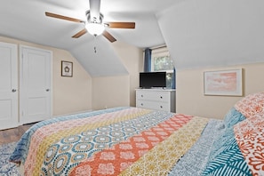 A bedroom with a bed, a ceiling fan, a dresser, a television, and a window with blinds.