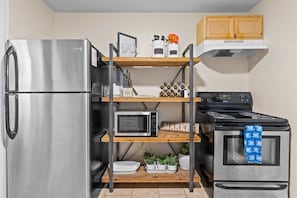 Une cuisine compacte équipée d’un réfrigérateur en acier inoxydable, d’un four à micro-ondes, d’une cuisinière et d’une étagère contenant divers ustensiles de cuisine.