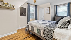 Quarto com cama, ventilador de teto, janela com cortinas e um quadro na parede.