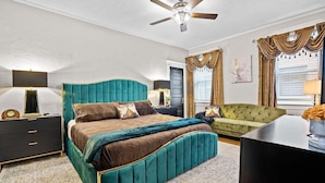 Ein Schlafzimmer mit einem großen Bett, einem grünen Sofa, einer schwarzen TV-Konsole und einem Deckenventilator.