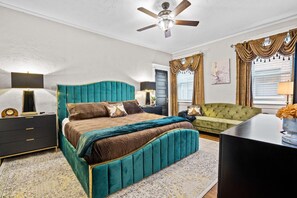 A bedroom with a large bed, a green sofa, a black desk, and a ceiling fan.
