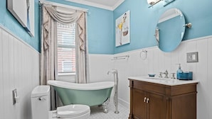 Ein Badezimmer mit freistehender Badewanne, Toilette in Weiß, einem Holzwaschtisch mit Spiegel und blauer Wand.
