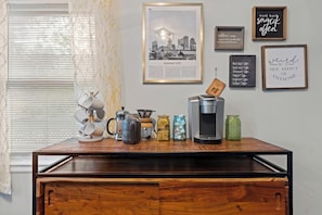 A coffee station with a coffee maker, a kettle, and various mugs on a wooden table.