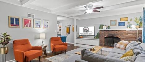 A living room with a fireplace, two orange armchairs, a grey sofa, and a ceiling fan.