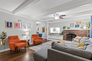 A living room with a fireplace, two orange armchairs, a grey sofa, and a ceiling fan.