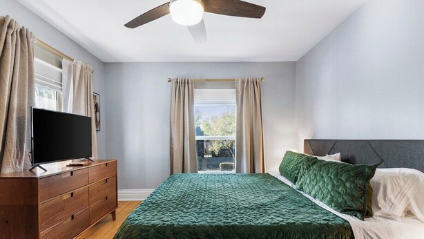 Une chambre à coucher comprenant un lit, une commode, un téléviseur et un ventilateur de plafond.