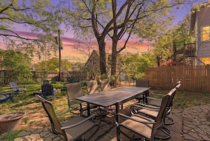 A patio with a table and chairs, surrounded by trees and a wooden fence.