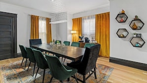Uma sala de jantar moderna com uma mesa de madeira grande, cadeiras estofadas em verde e um lustre.