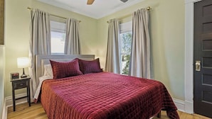 Quarto com cama, mesa de cabeceira, luminária, ventilador de teto e porta.