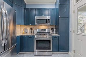 A kitchen with dark blue cabinets, stainless steel appliances, and a granite countertop. - Beautiful Westport Manor - Remodeled with 3 King beds! (Kansas City)