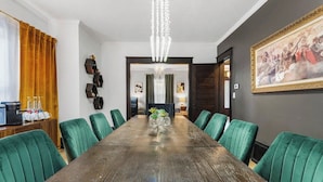 Une salle de conférence avec une longue table, des chaises recouvertes d’un tissu vert, un lustre et des œuvres d’art accrochées aux murs.